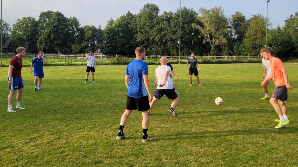 Acht Männer beim Fußballtraining auf dem Rasenplatz, zwei Spieler kämpfen um den Ball im Vordergrund.