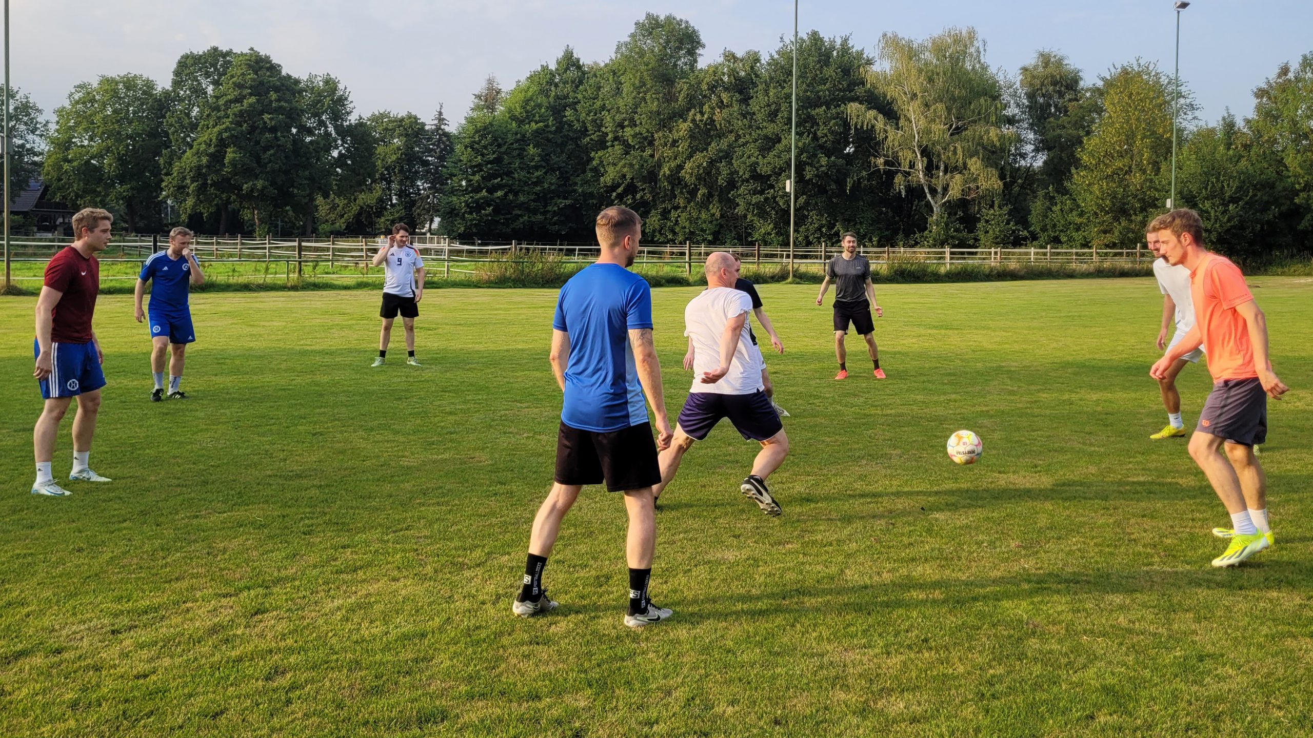 Acht Männer beim Fußballtraining auf dem Rasenplatz, zwei Spieler kämpfen um den Ball im Vordergrund.