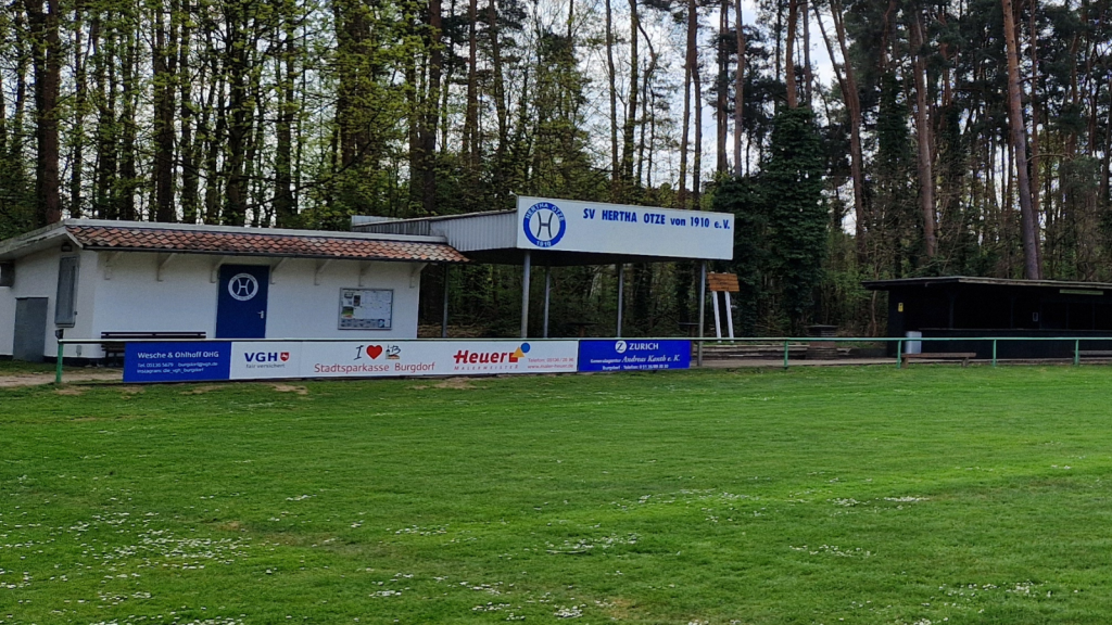Blick auf das Vereinsheim des SV Hertha Otze mit umliegender Bandenwerbung verschiedener lokaler Unternehmen.