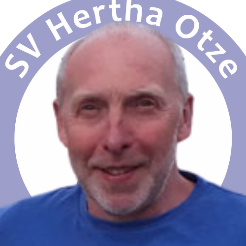 Portrait von Friedhelm Döbel vor dem Logo des SV Hertha Otze. Er trägt ein blaues Shirt und lächelt freundlich in die Kamera.