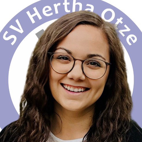 Julia Herburg, lachend, vor dem Logo des SV Hertha Otze
