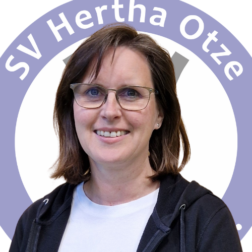 Portrait von Kirsten Buchholz vor dem Logo des SV Hertha Otze. Sie trägt eine Brille, ein weißes T-Shirt mit schwarzer Jacke und blickt freundlich in die Kamera.