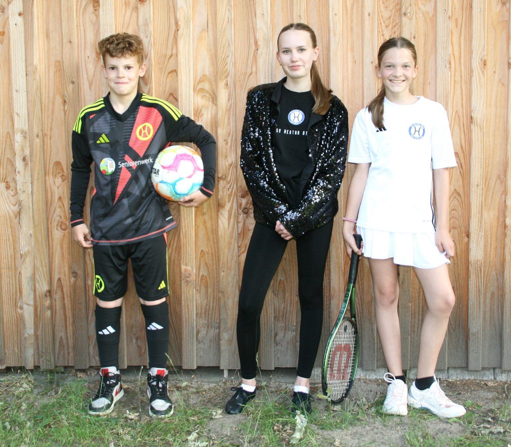Drei Jugendliche des SV Hertha Otze stehen vor einer Holzfassade: Ein Junge in Fußballtrikot mit Ball, ein Mädchen in schwarzer Trainingskleidung mit Paillettenjacke und ein Mädchen im weißen Tennisoutfit mit Tennisschläger.