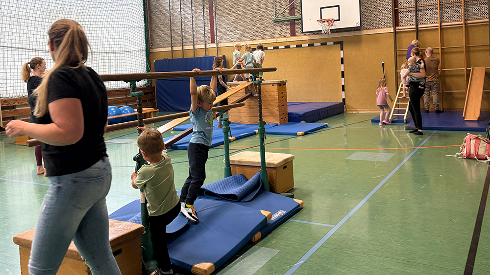 Kinder und Eltern beim gemeinsamen Turnen an Geräten wie Barren und Kletterwand.