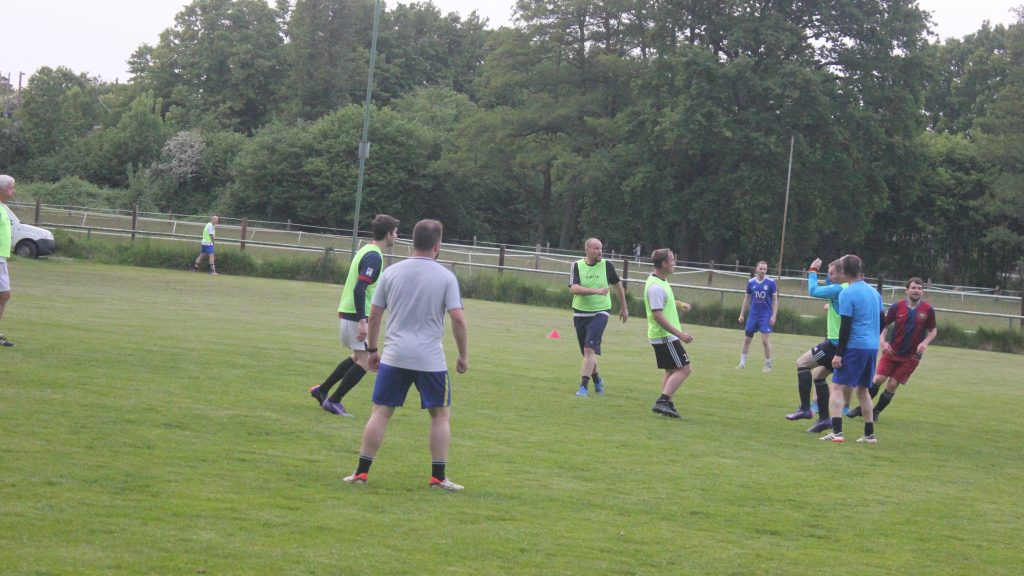 Freizeitkicker der Mannschaft „Otzes Hoffnung“ beim Spiel auf dem Rasenplatz des SV Hertha Otze. Die Spieler in grünen Leibchen und farbigen Trikots sind in Bewegung und im Zweikampf um den Ball.