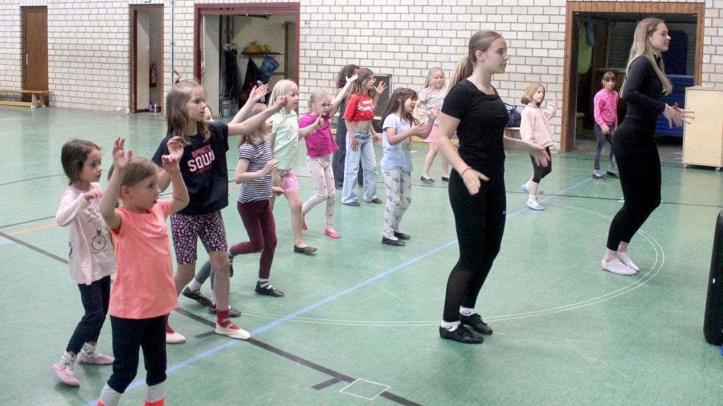 Mädchen der Tanzgruppe „Sternchen“ tanzen gemeinsam mit zwei Übungsleiterinnen in der Sporthalle