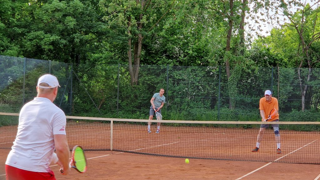 Drei Männer beim Tennisspielen auf einem Sandplatz im Grünen