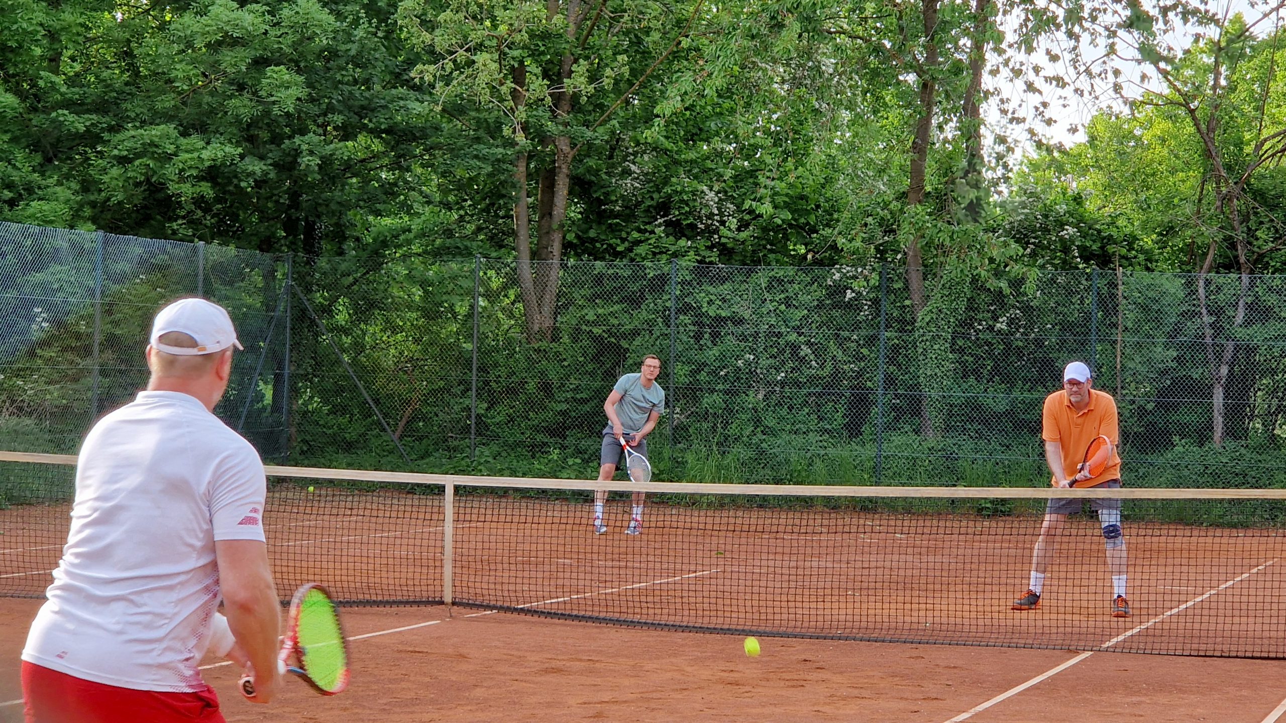 Drei Männer beim Tennisspielen auf einem Sandplatz im Grünen