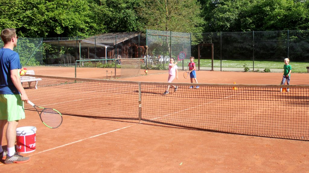 Kinder beim Tennistraining auf einem Sandplatz, betreut von einem Trainer