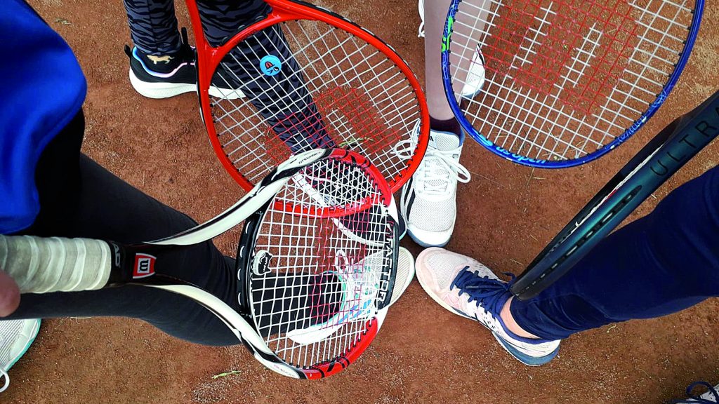 Mehrere Tennisschläger und Sportschuhe im Kreis von oben fotografiert