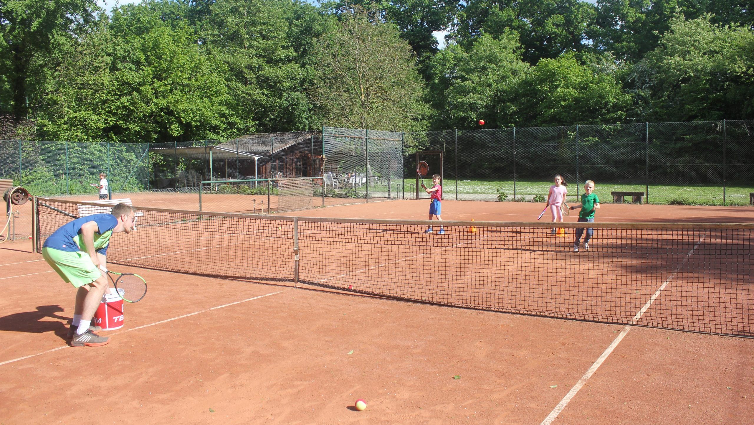 Kinder trainieren mit Tennisschlägern auf einem Sandplatz unter Anleitung eines Trainers.